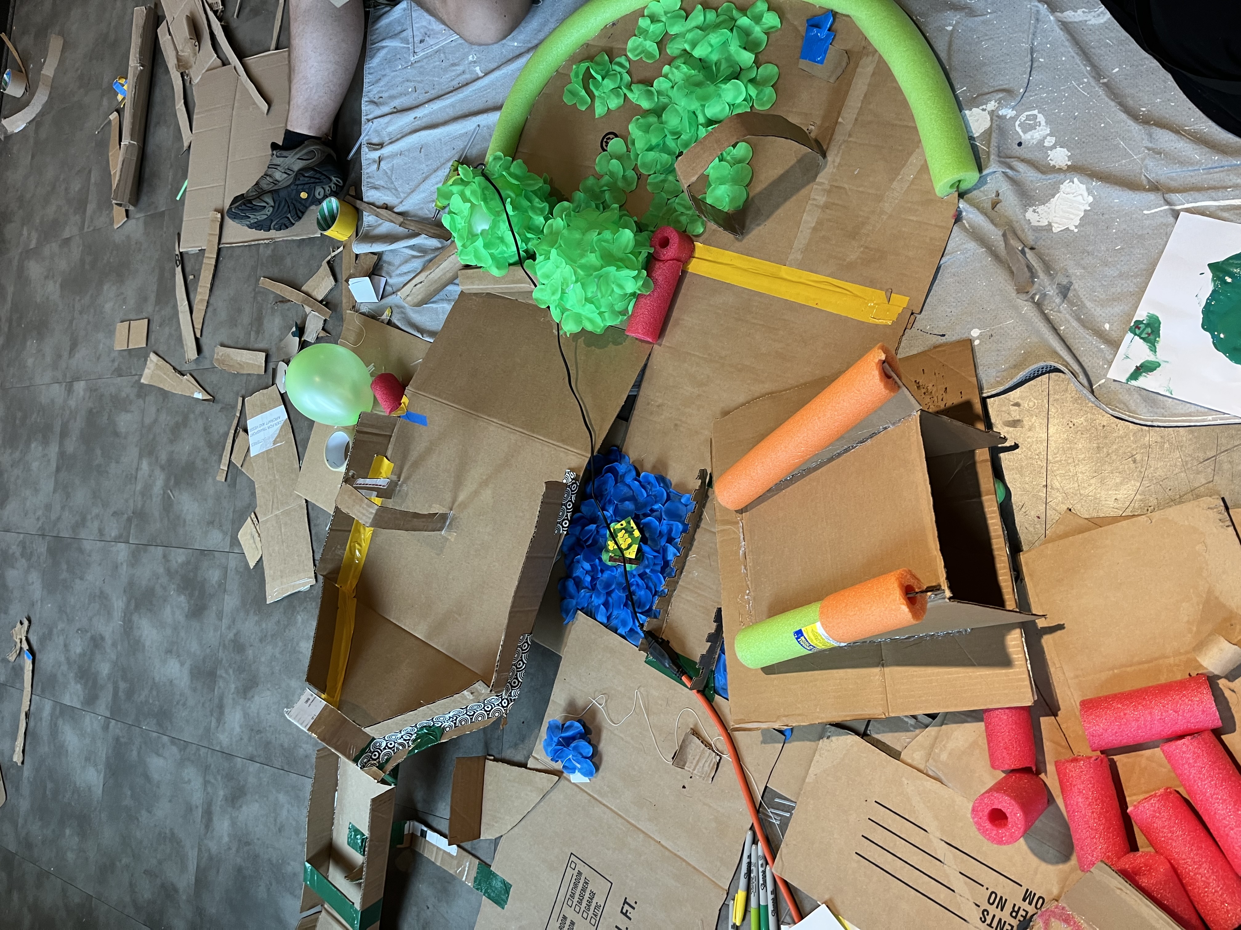 a croquet slash golf course, incorporating details from both games. Our design in this picture has a bridge with water made out of fake blue petals, balloon trees, and an upward slope at the end. You can also see the mess around it from the work.